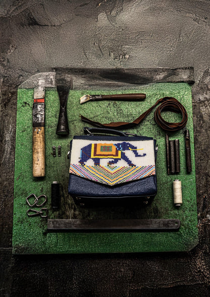 Royal blue elephant motif in Czech glass beads on a structured bag next to its specialized manufacturing tools.
