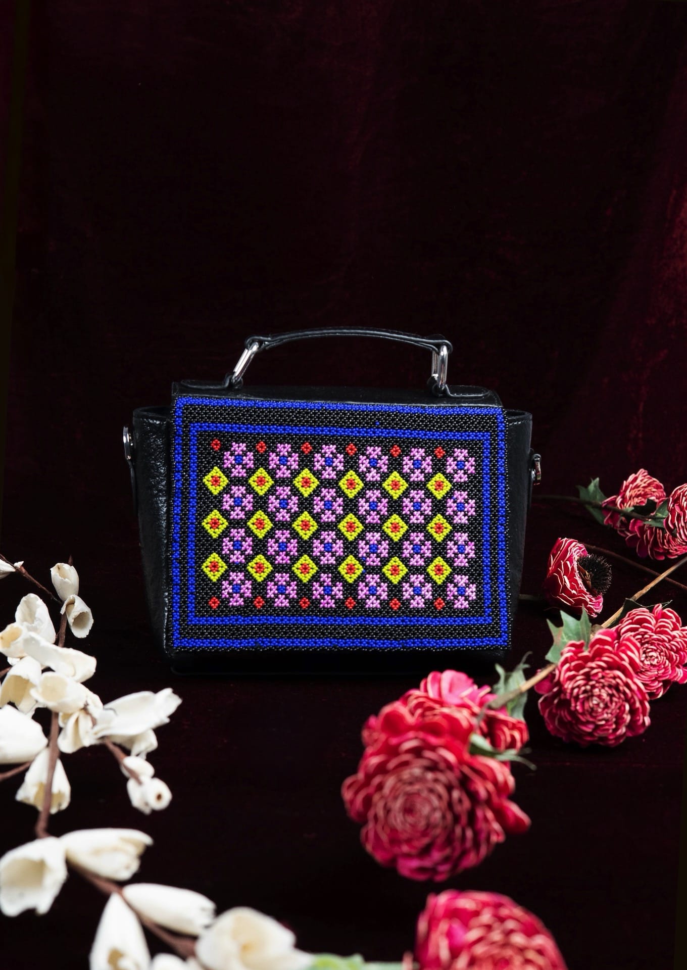 Intricate Czech glass geometric beadwork framed by cobalt blue next to flowers, authentic Gujarati artisan bag.