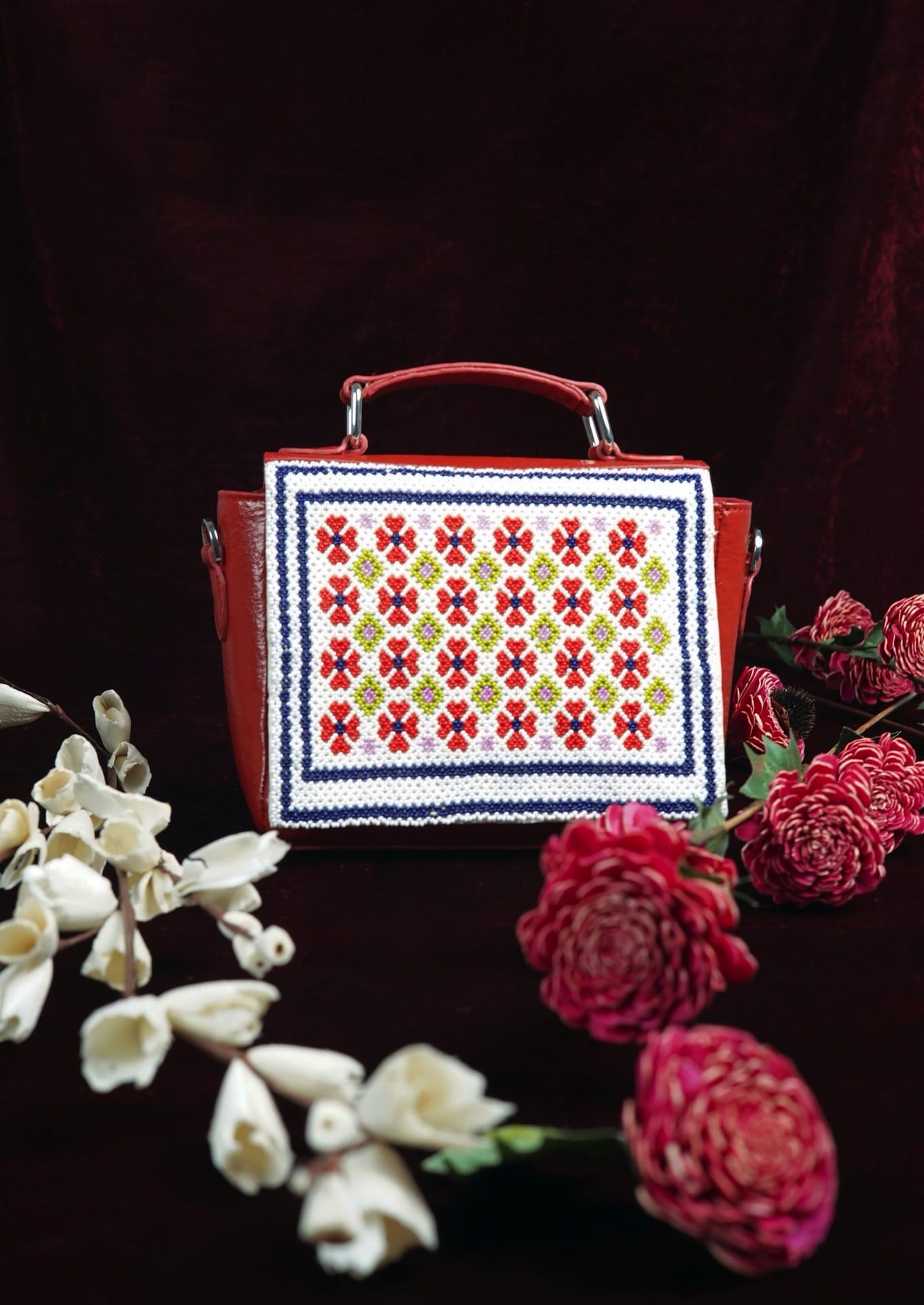 Symmetrical Czech glass bead flowers on a bright red handbag next to flowers on a red background, authentic Gujarati dal-moti craft.