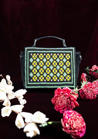 Geometric Czech glass bead patterns on a black structured bag surrounded by flowers, traditional Saurashtra handicraft.