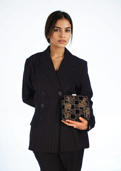 Woman in a black pinstripe suit holding an intricate golden beadwork motifs on a sophisticated black clutch, authentic Lucknow fashion.