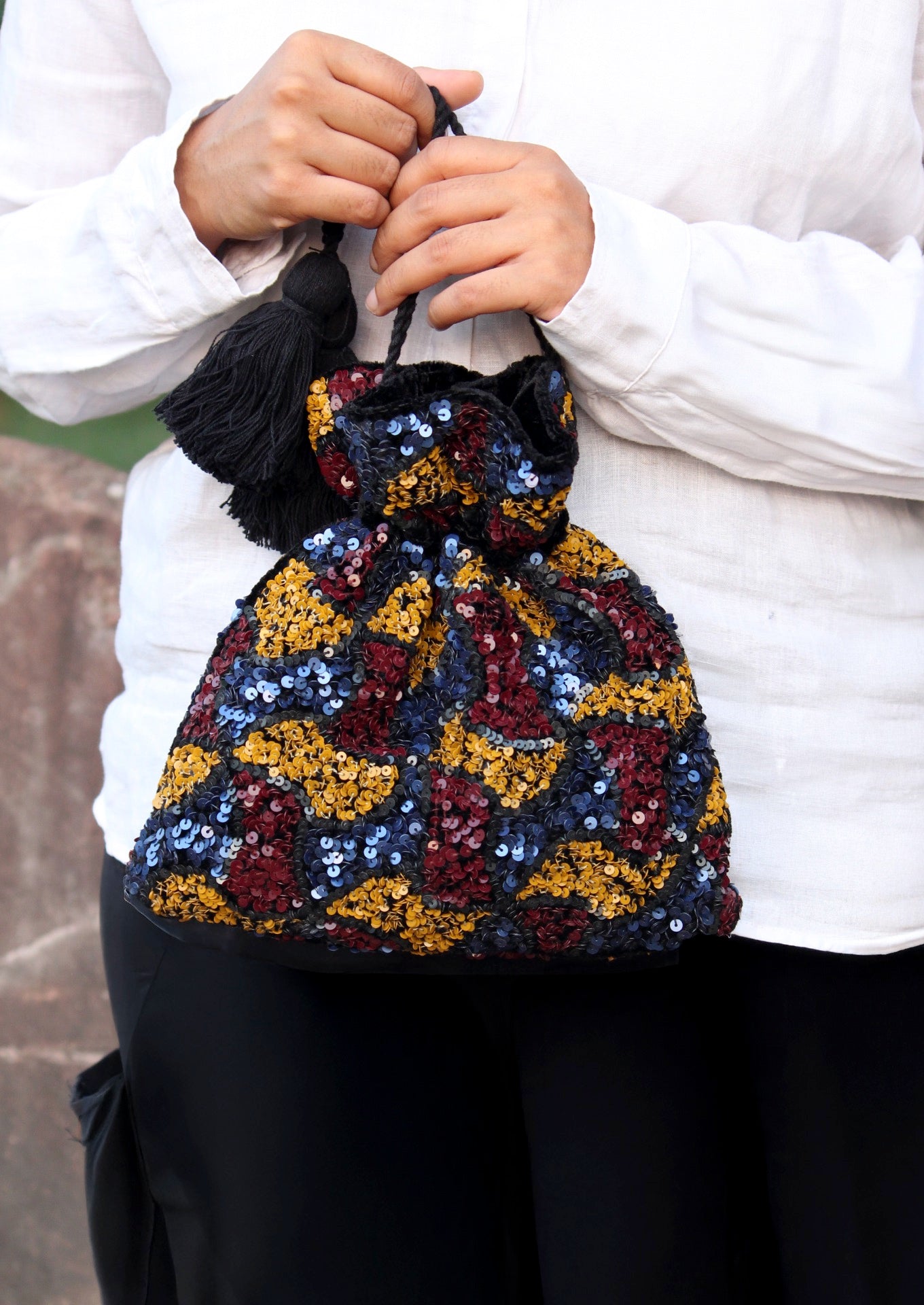 Handcrafted recycled velvet potli bag with a long string handle, luxury Indian accessory held by a person.