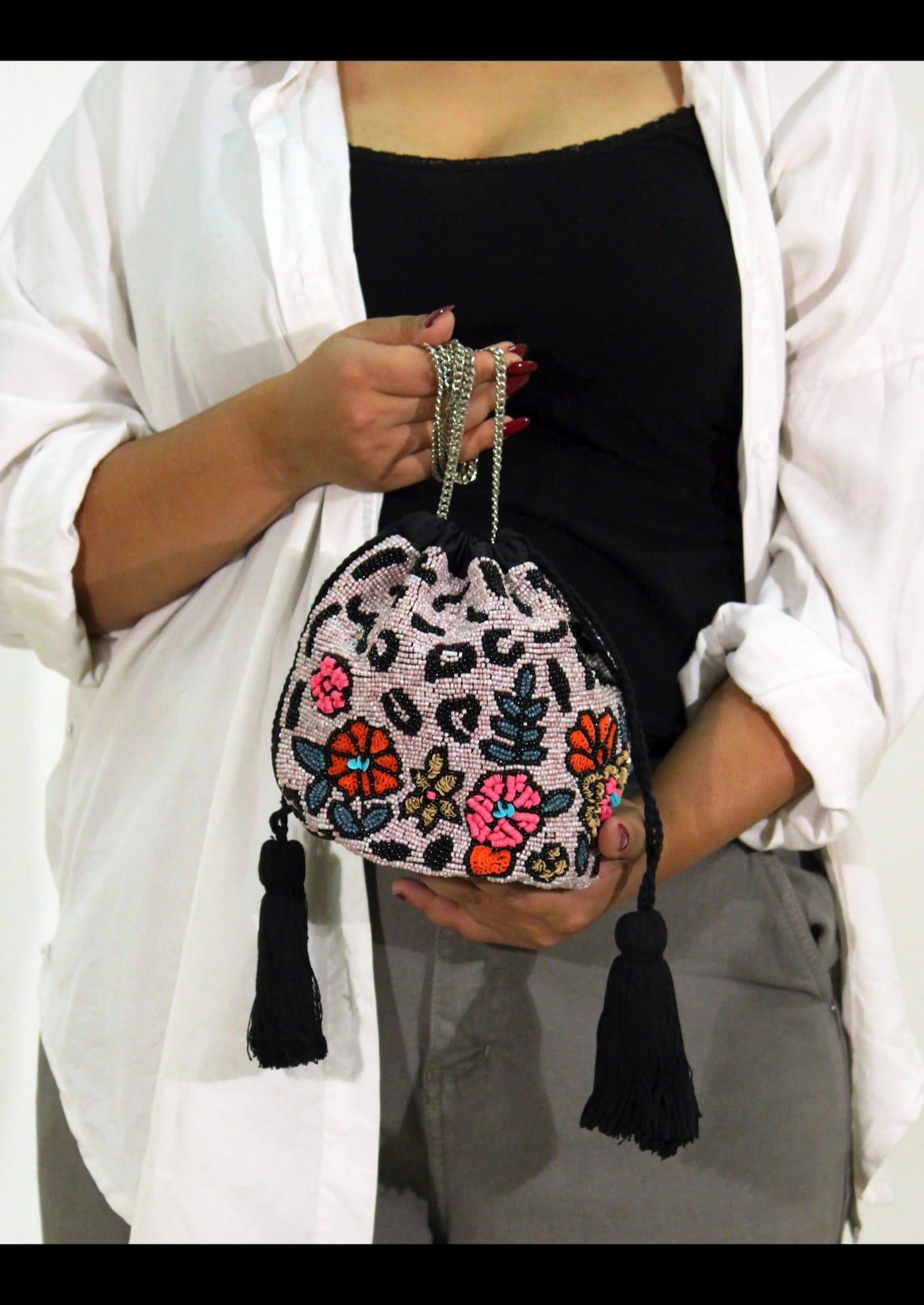Person holding a colorful beaded handbag with floral patterns and tassels.